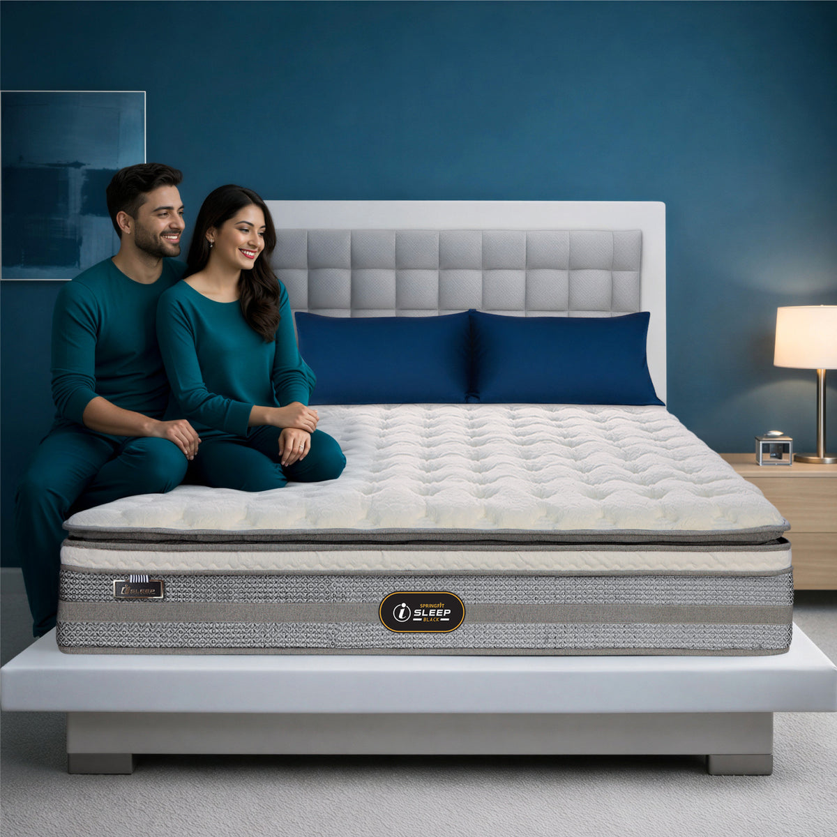 Springfit iSleep Black mattress on a white platform bed with a smiling couple seated together in a vibrant blue-toned modern bedroom