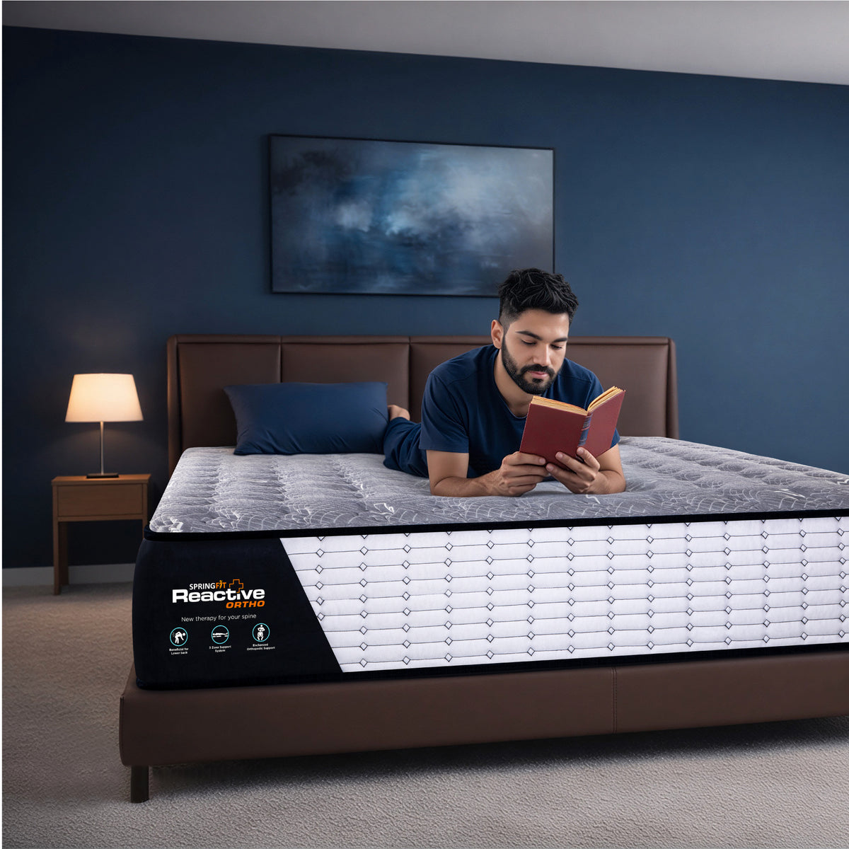 Springfit Reactive Ortho orthopedic mattress lifestyle image with man in navy outfit reading a book while lying on mattress on brown leather bed in dark blue accent bedroom with side lamp